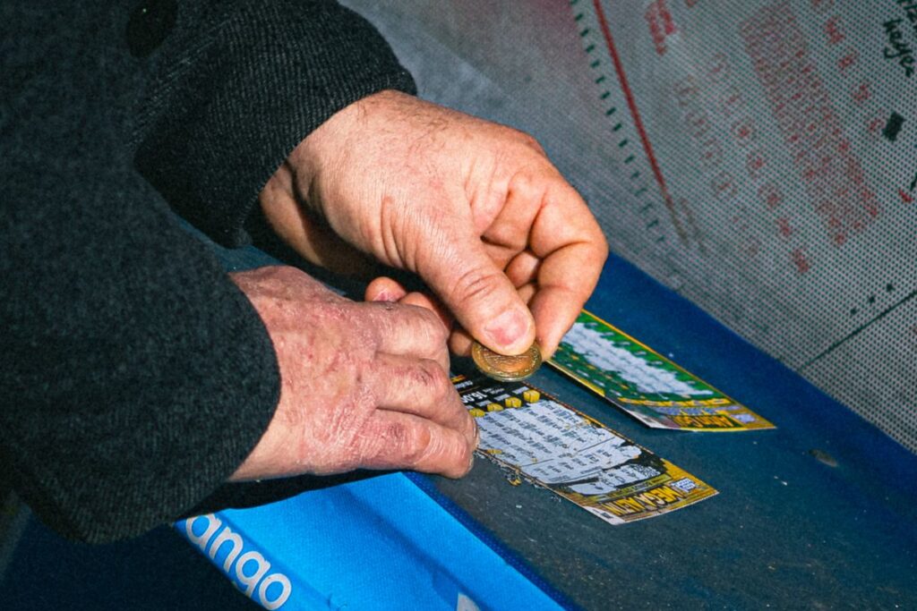 Spar-Aktion Rubbeln: Hände rubbeln ein Rubbellos mit einer Münze frei